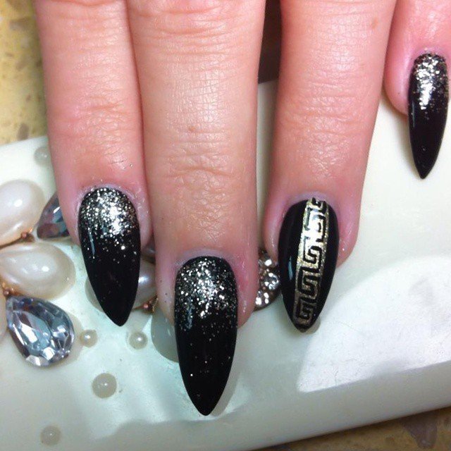Stylish black nails with gold glitter and intricate geometric designs on a manicured hand.