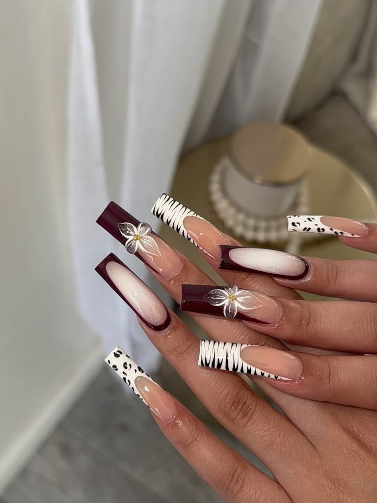 Stylish long acrylic nails with maroon, animal print, and floral designs. Perfect for a trendy and bold look.