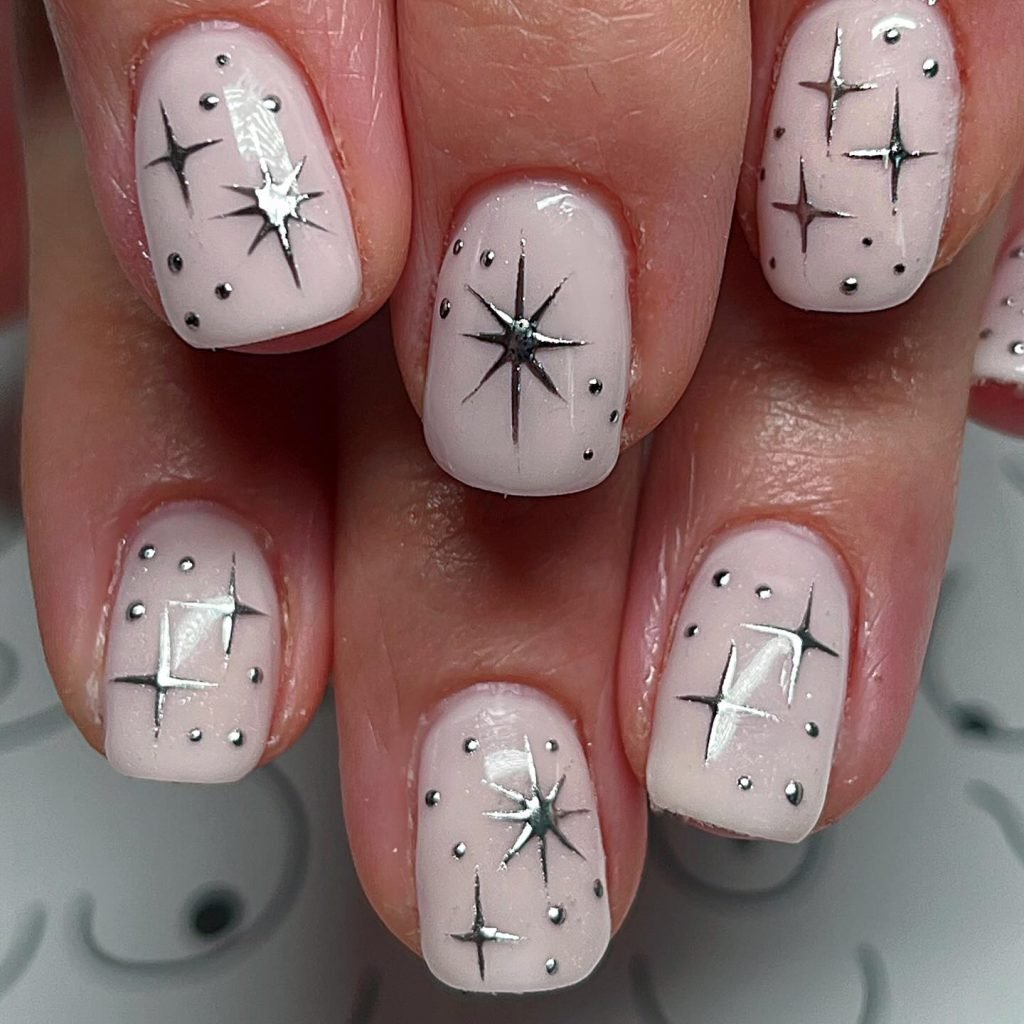 Light pink nails with silver star designs and dotted accents for a chic, celestial nail art look.