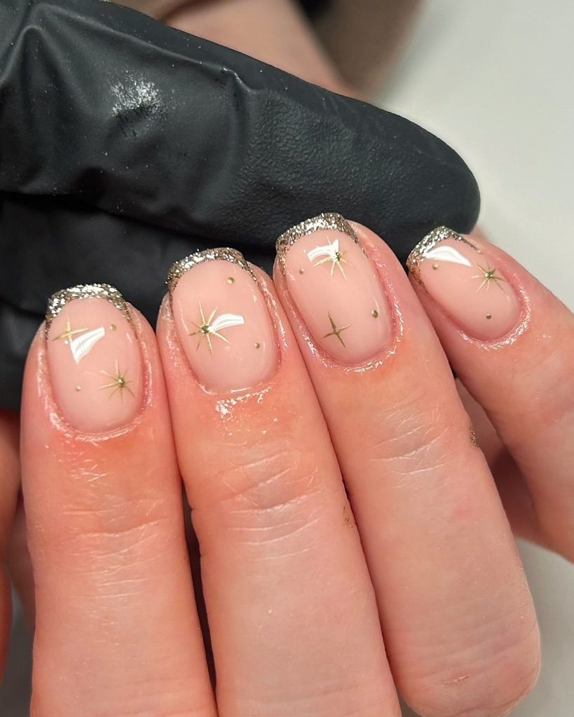 Nude nails with glittery silver tips and starry gold designs, creating elegant and festive nail art.