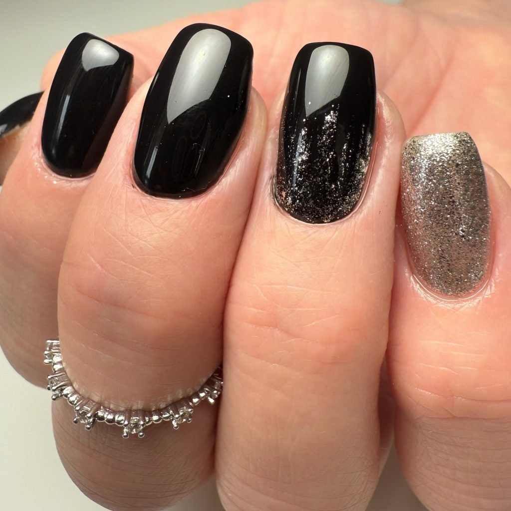 Silver and black glitter manicure with a beaded ring on a hand, showcasing elegant and stylish nail art.