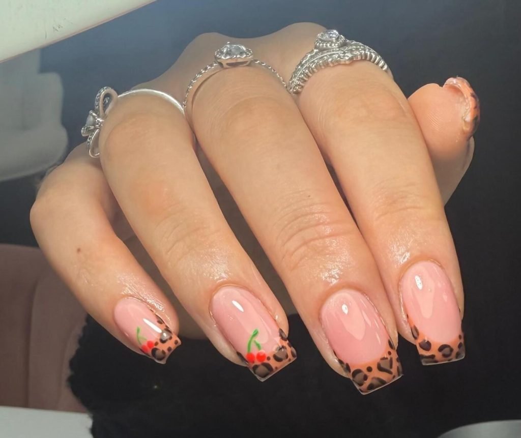 Pink manicure with leopard and cherry nail art design and silver rings on fingers.