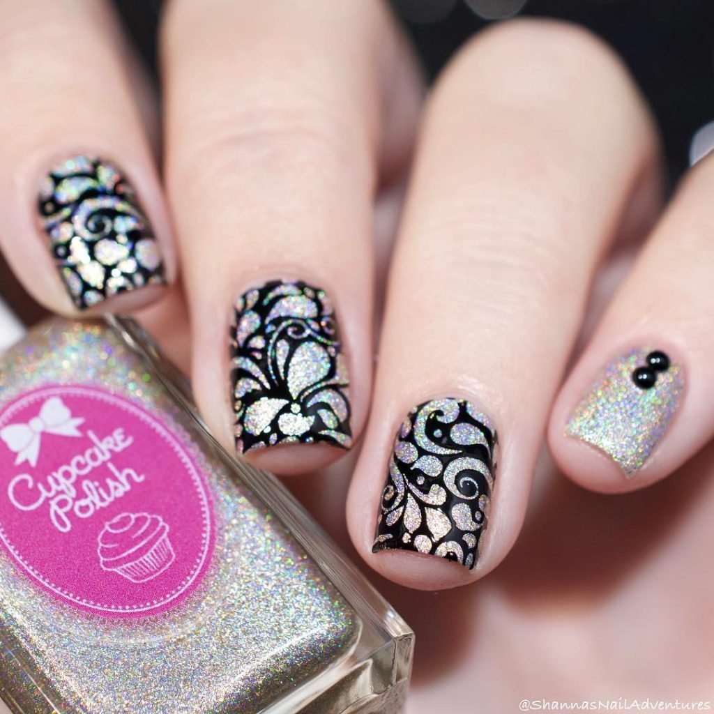 Holographic nail polish with intricate black lace design and a bottle of Cupcake Polish in close-up.