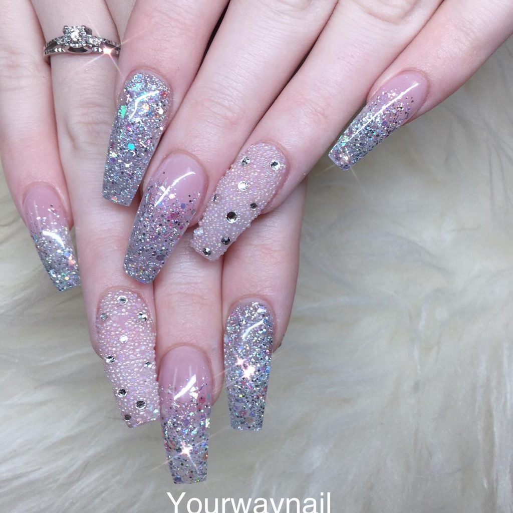 Glittery long acrylic nails with rhinestones on a beige fur background.