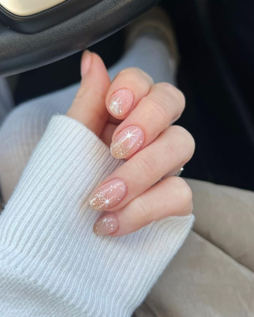 Elegant nude nails with glittery tips and star accents on a hand in a cozy white sweater, perfect winter nail art.