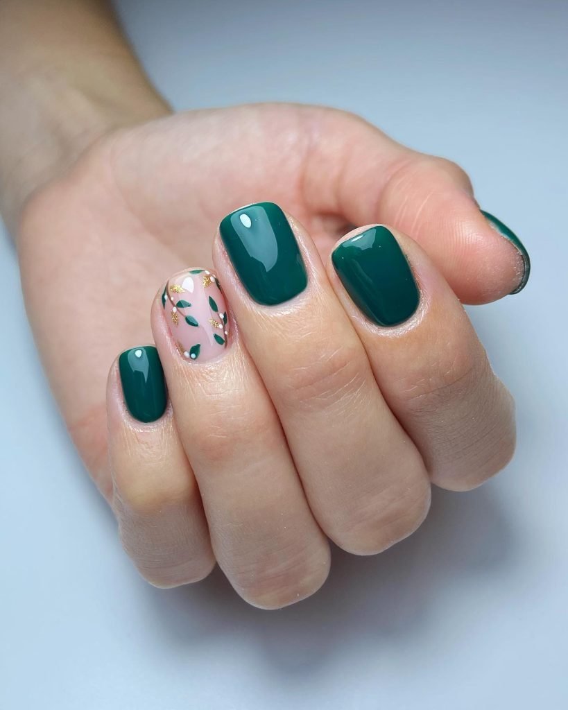 Hand with stylish green manicure and accent nail art featuring leaf designs on light pink background.