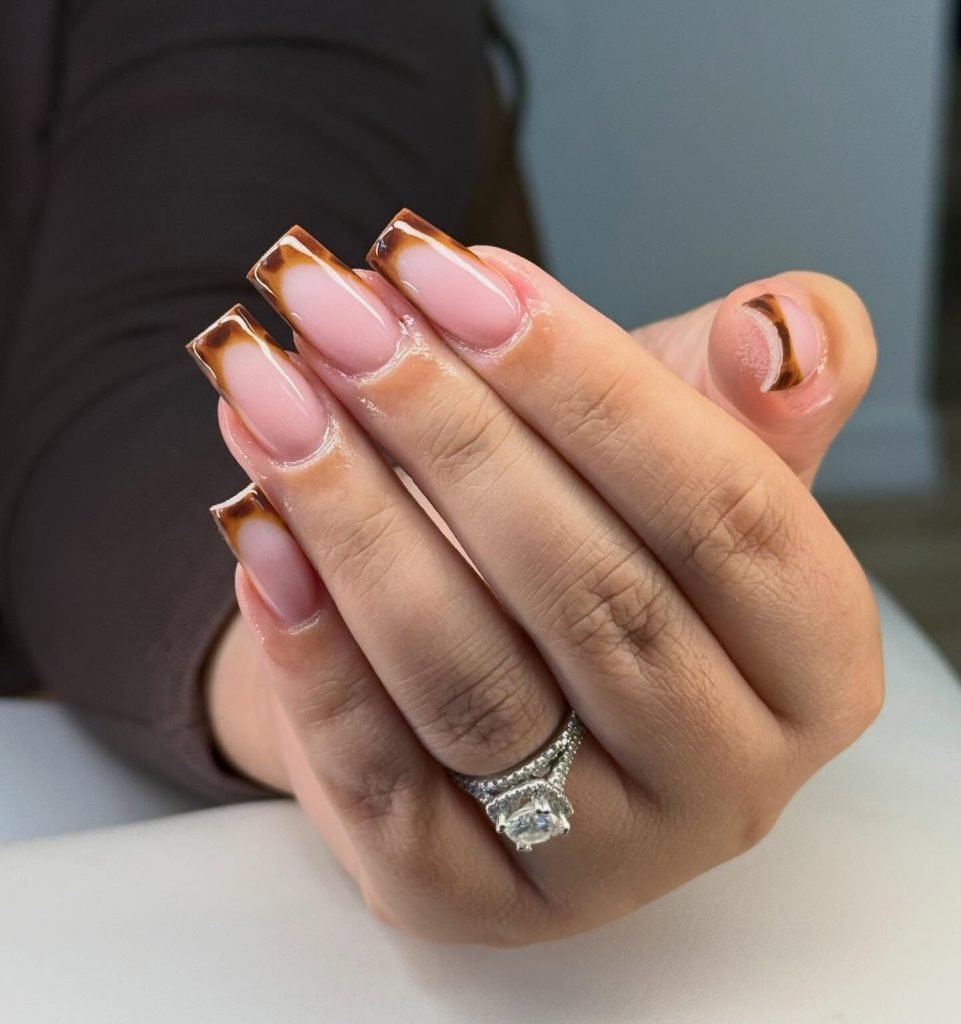 Close-up of hand with brown tortoiseshell nail art and diamond ring. Elegant manicure showcasing trendy nail design.