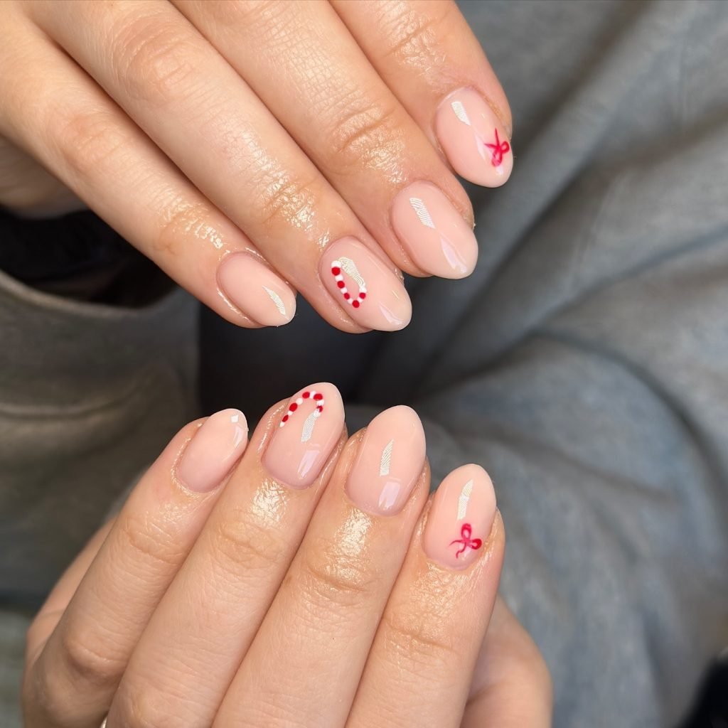 Elegant nude nails with red bows and polka dot accents, showcasing festive and stylish nail art design.