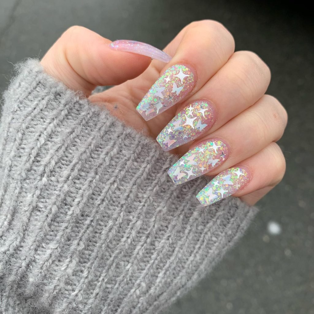 Sparkly holographic star nails with a cozy gray sweater in the background. Trendy manicure inspiration.