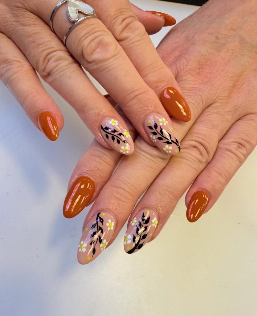Autumn-inspired nail art with orange polish and floral designs on beige nails, showcasing elegant fall manicure trends.