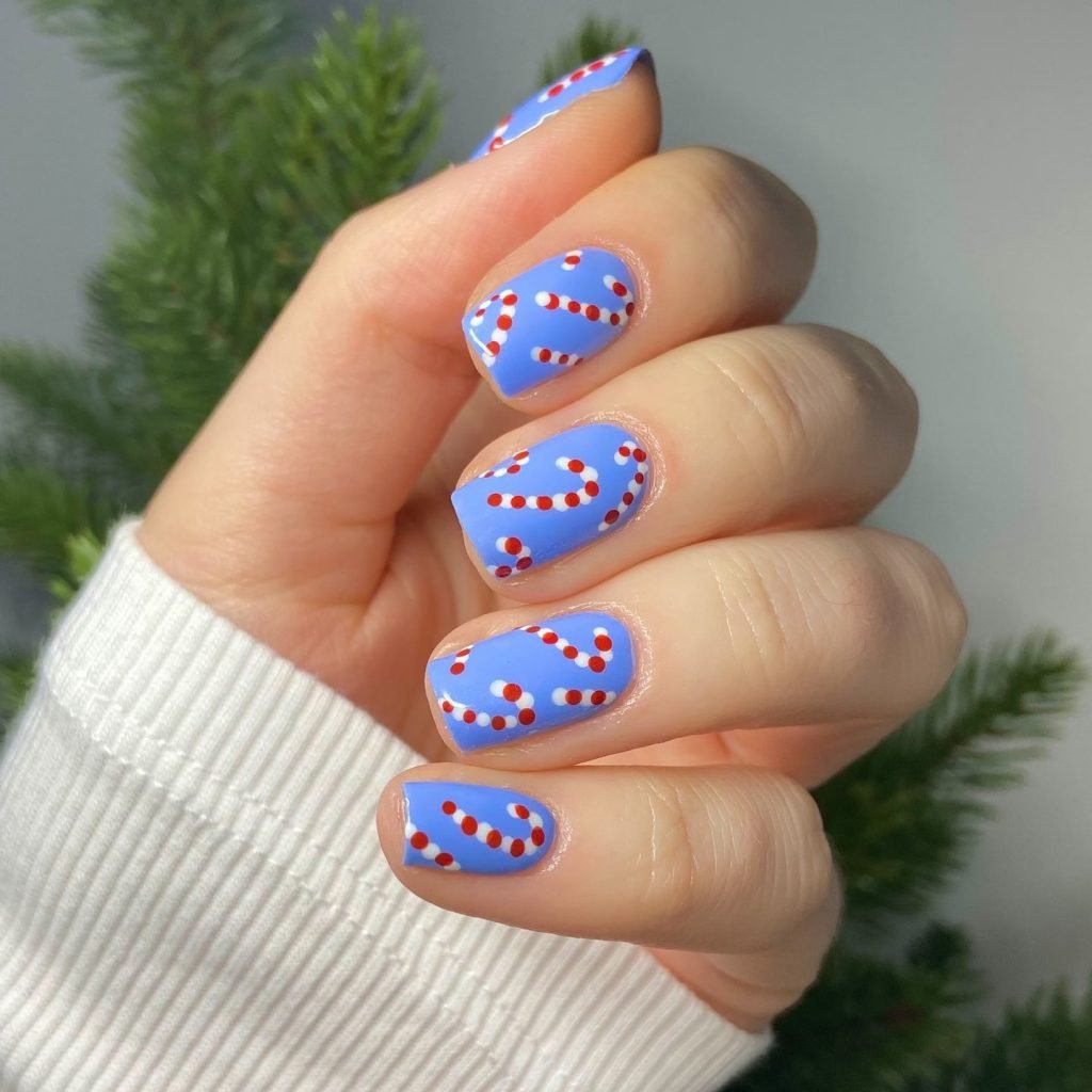 Blue nails with red and white polka dot design, set against a white sweater and green background.