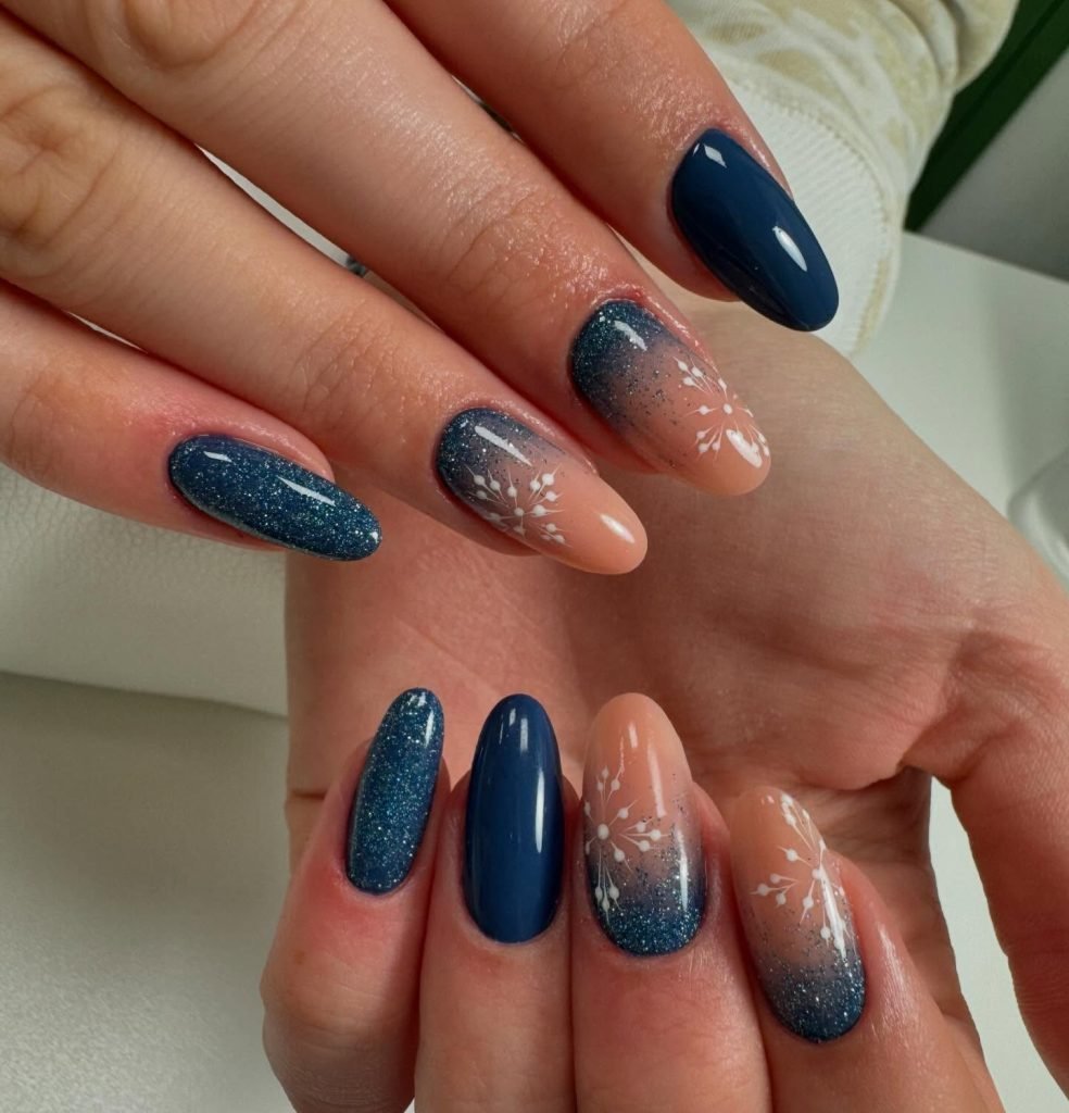 Navy and nude gel nails with glitter and white snowflake designs, showcasing winter-themed nail art.