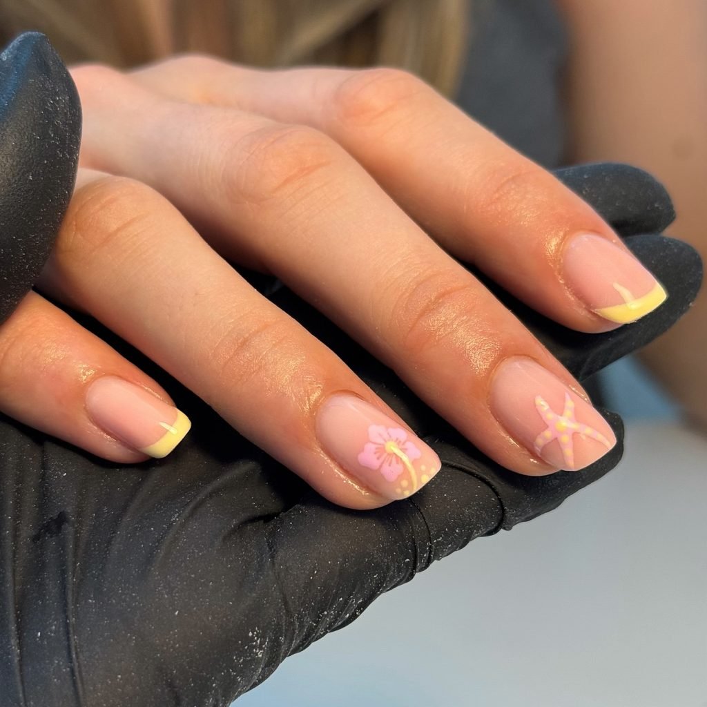 Pastel floral nail art with yellow tips on a manicured hand, showcased by a gloved technician.