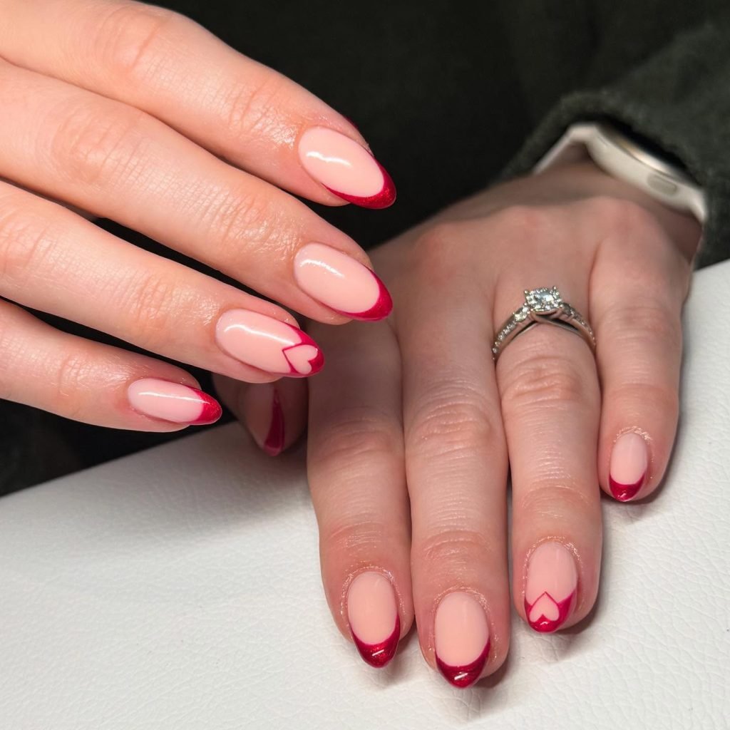 Elegant red French tip manicure with heart design, worn with a diamond ring on a white surface.