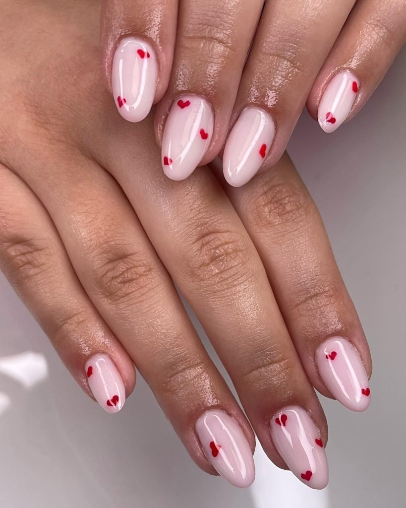 Elegant pink nails with tiny red heart designs, showcasing a cute and romantic manicure style.