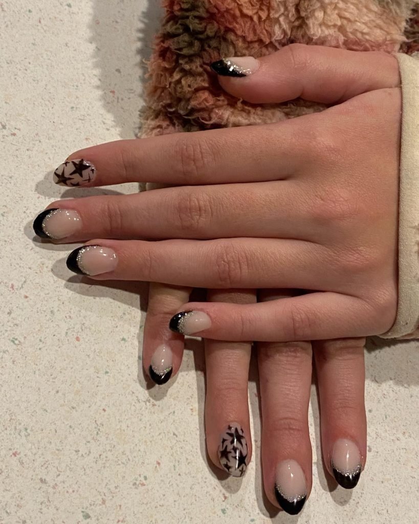 Close-up of hands with stylish black and white star-themed nail art on a textured surface.
