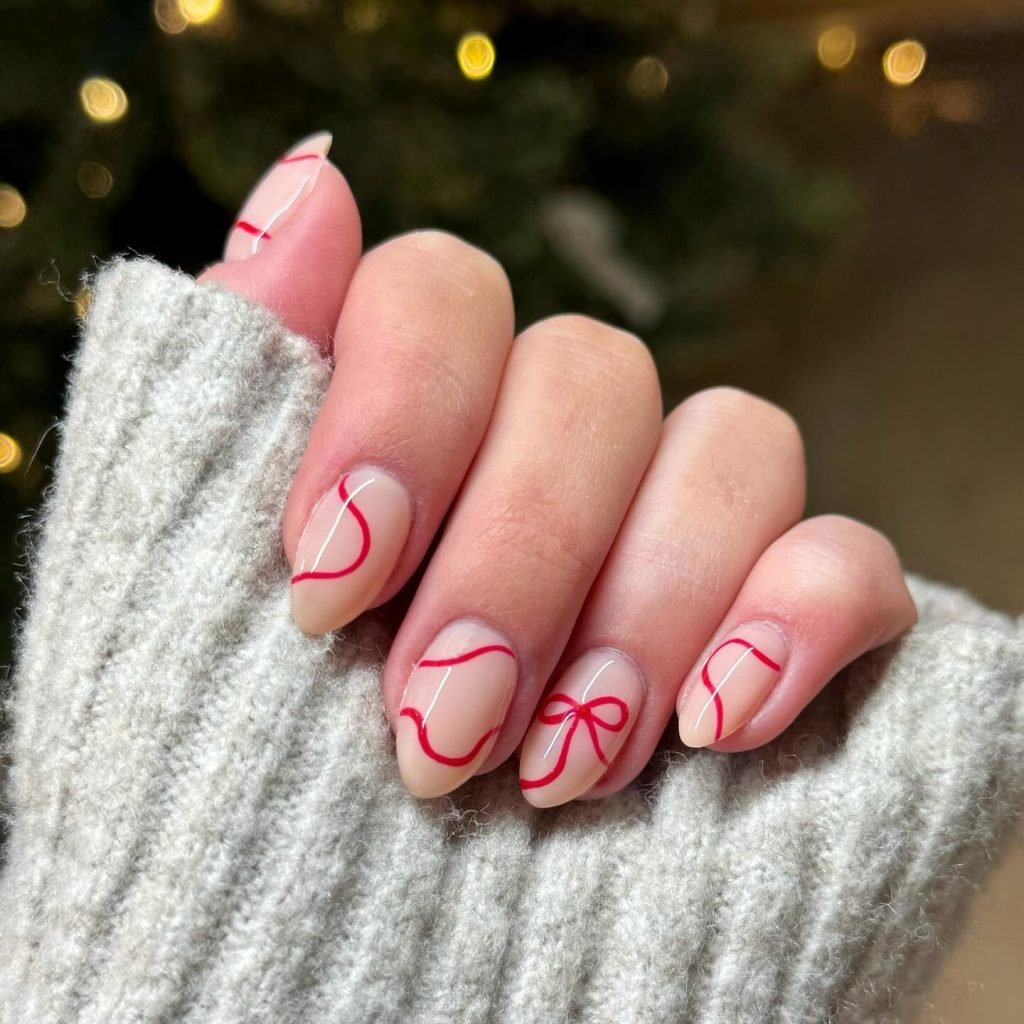 Festive nail art with red ribbons on a hand in a cozy sweater, perfect for holiday season inspiration.