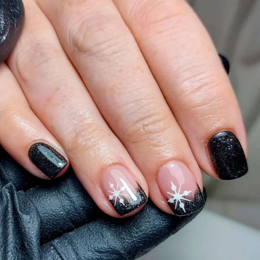 Black and nude manicure with white snowflake designs on two nails, showcasing winter-themed nail art.