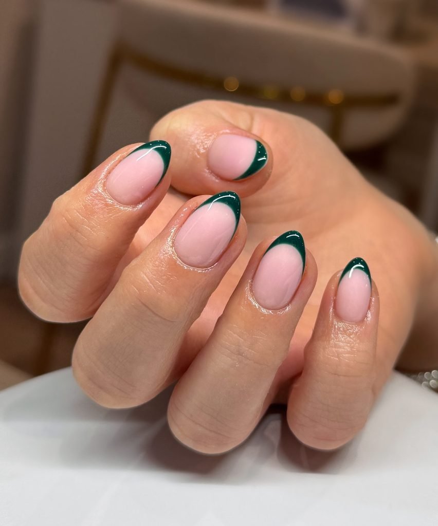 Close-up of hand with elegant dark green French tip manicure on nails.