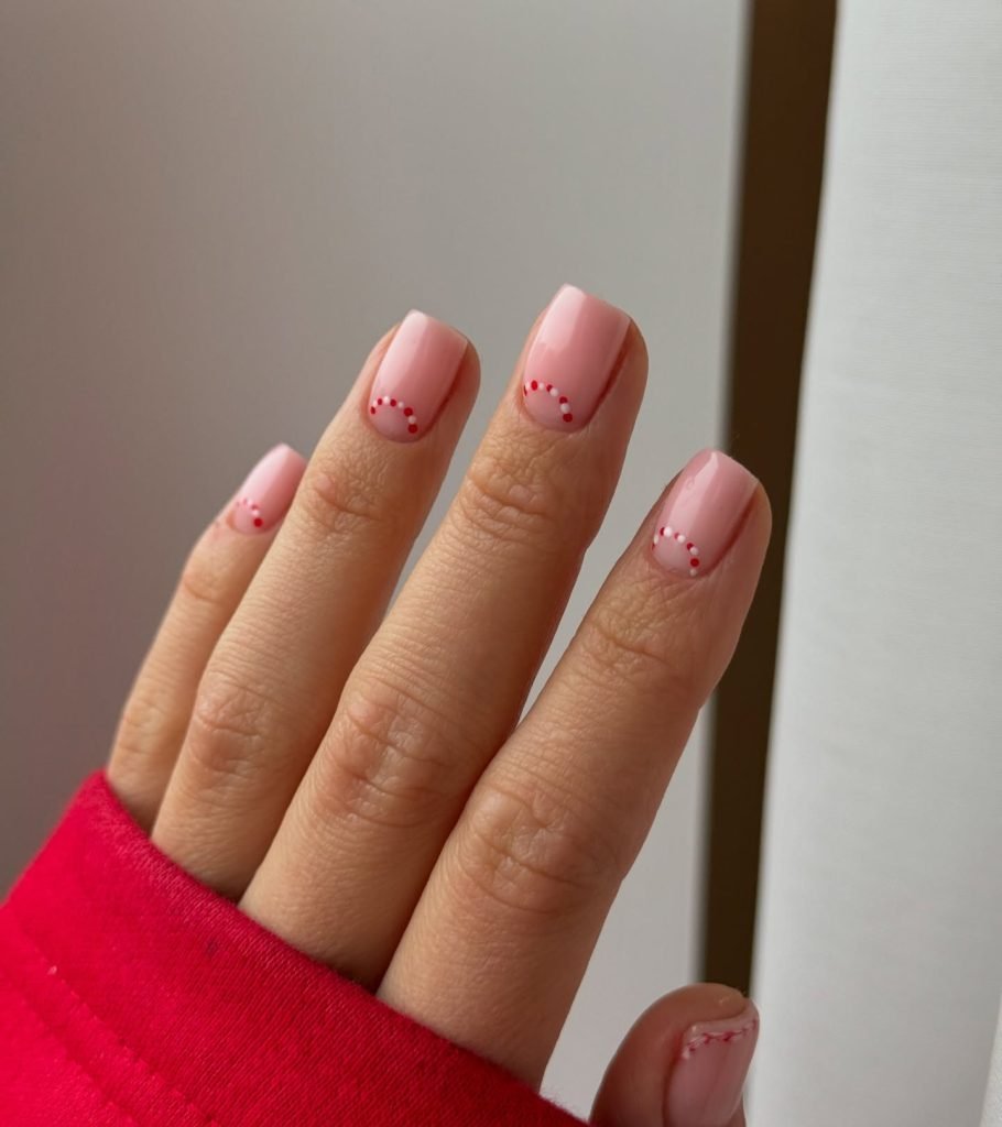 Soft pink manicure with red dotted design on short nails, thumb in red sleeve background.