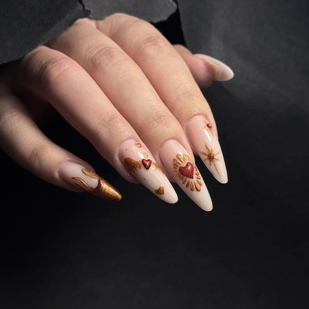Long stiletto nails with intricate gold and red heart designs on a black background, perfect for a bold nail art look.