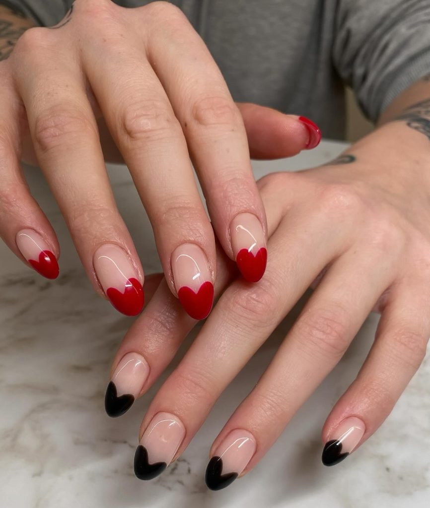 Colorful heart-themed nail art featuring red and black tips on a marble background. Trendy manicure style.
