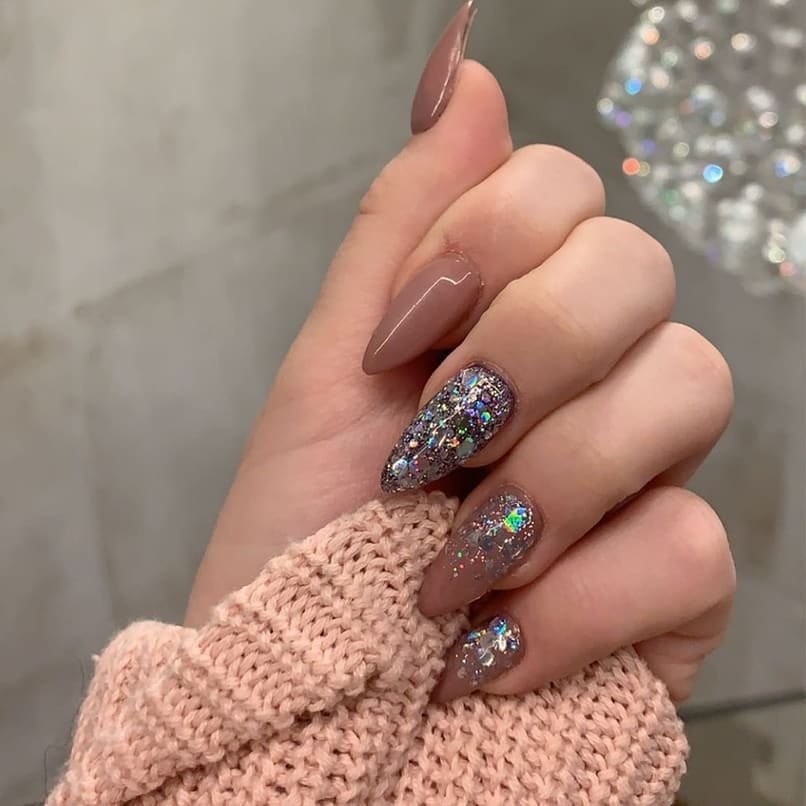 Close-up of manicured hand with nude and glitter nails, wearing a pink knitted sweater.