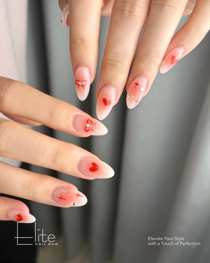 Elegant almond-shaped nails with red heart designs and rhinestones, adding a chic touch. Perfect for Valentine’s Day.