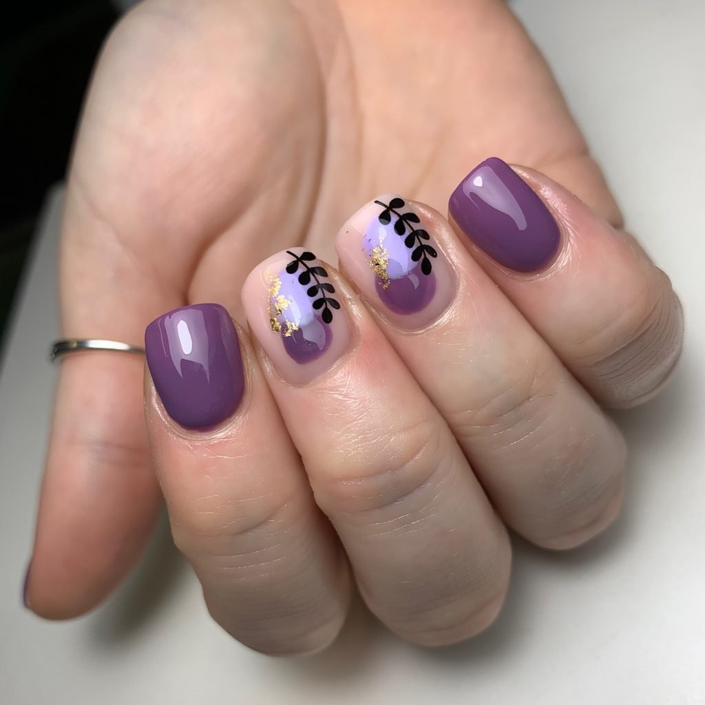 Purple and gold nail art with leaf accents on short, manicured nails.