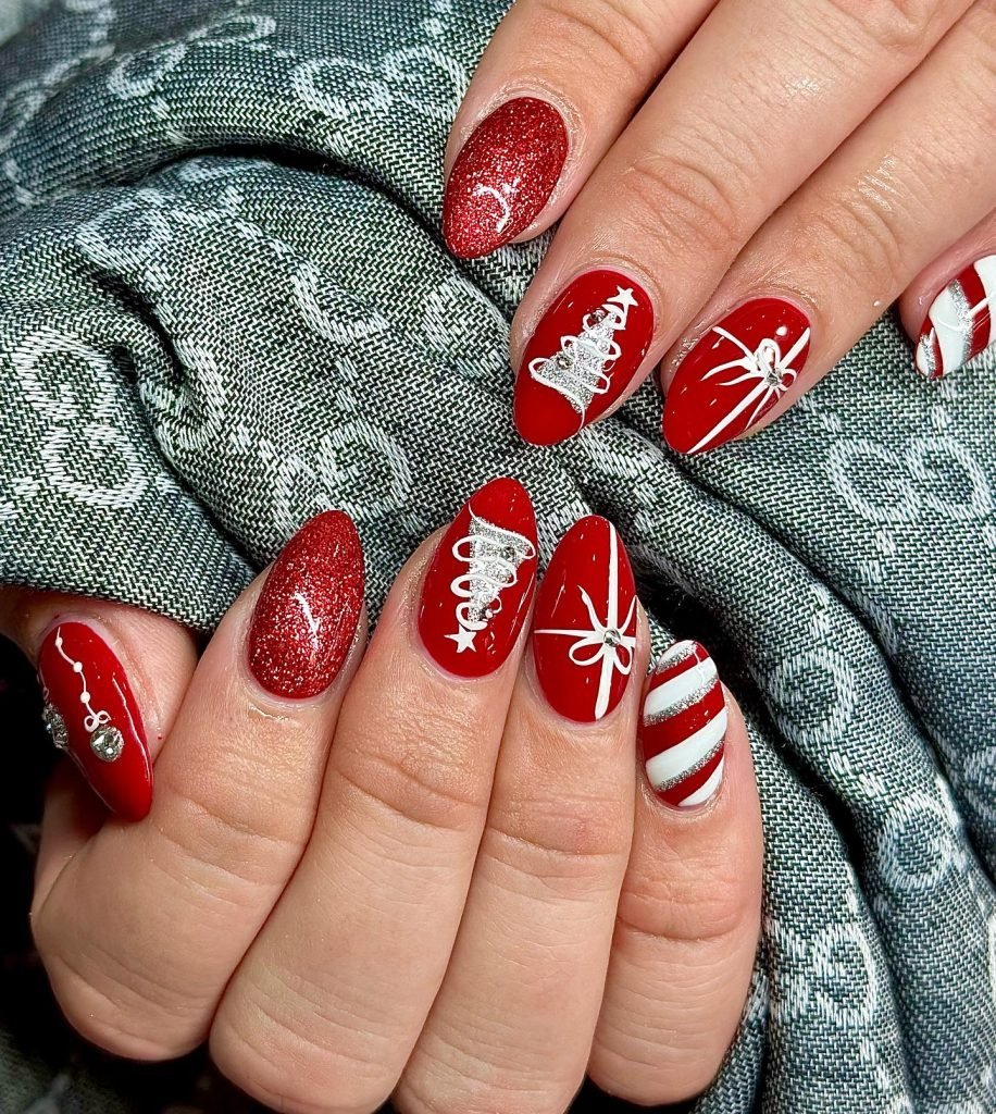 Festive red Christmas nail art with snowflakes, trees, and candy cane designs on manicured fingernails.
