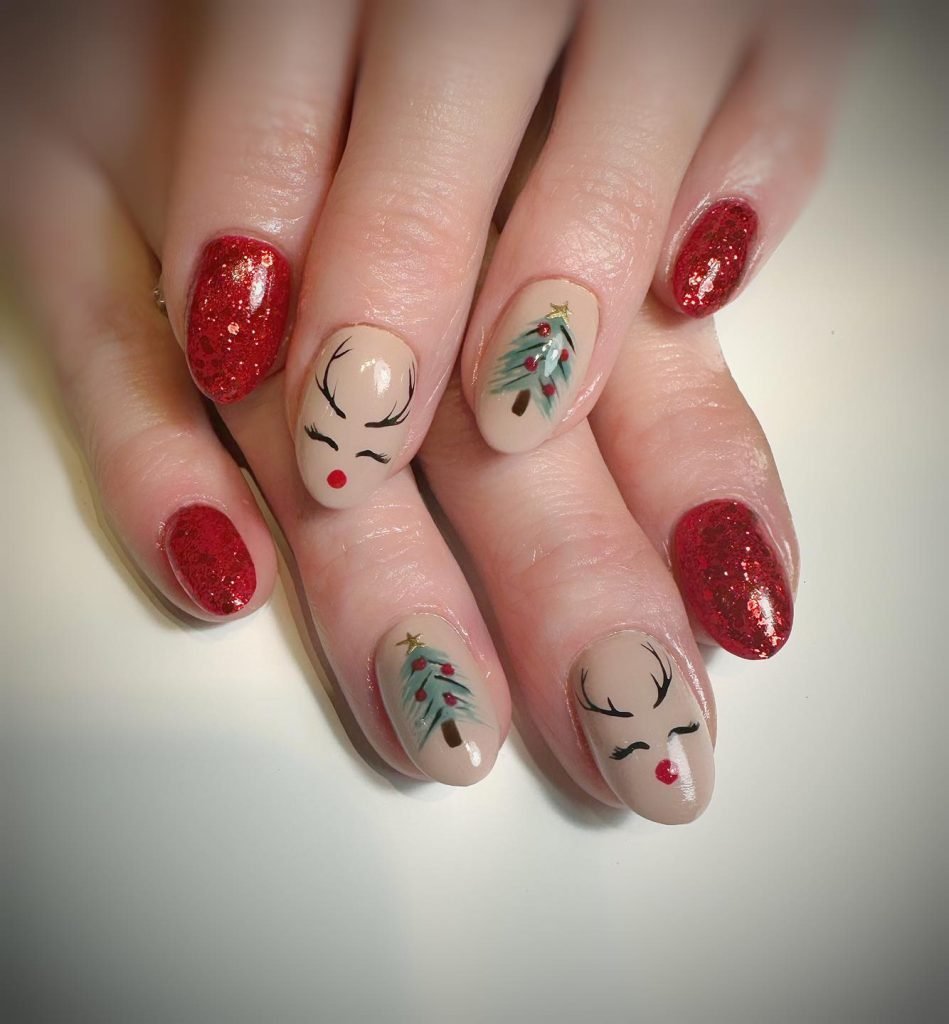Festive nail art with red glitter, reindeer, and Christmas tree designs on beige polish for a holiday theme.