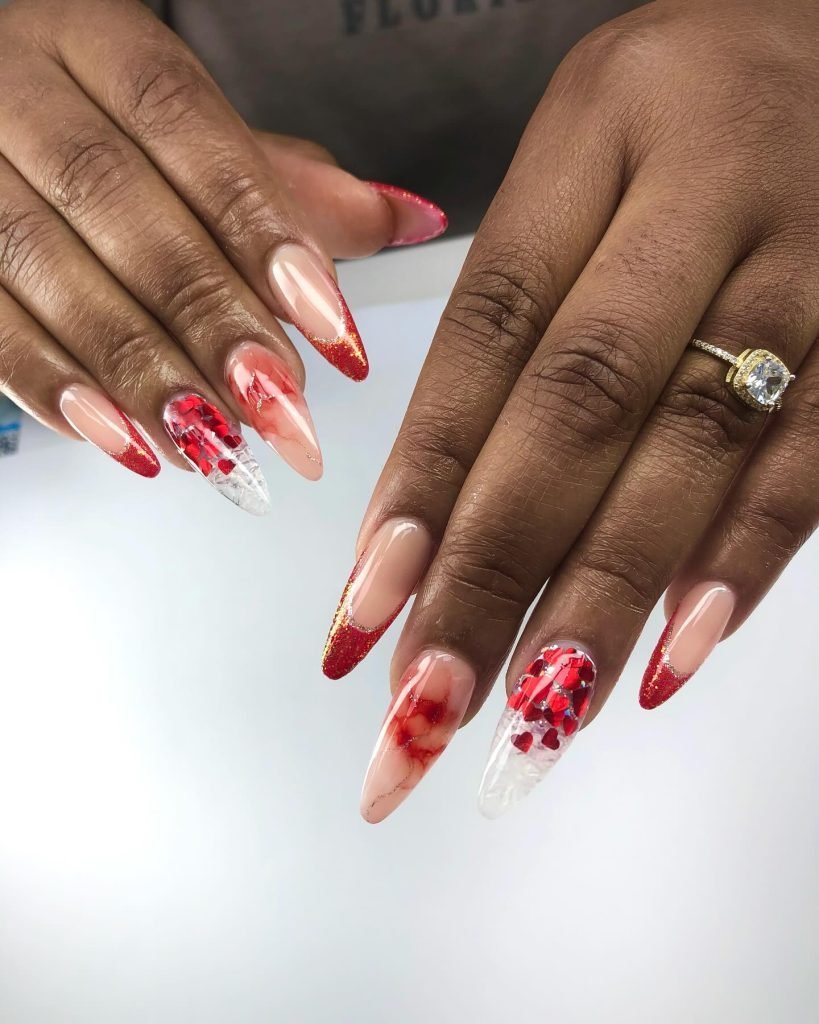 Stylish red and pink Valentine's Day nail art with hearts and glitter tips on almond-shaped nails.