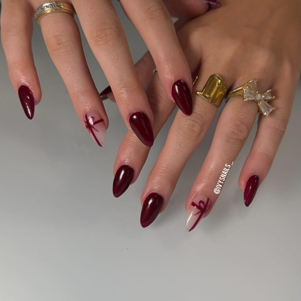 Stylish maroon and white stiletto nails with artistic design, adorned with gold rings on fingers.