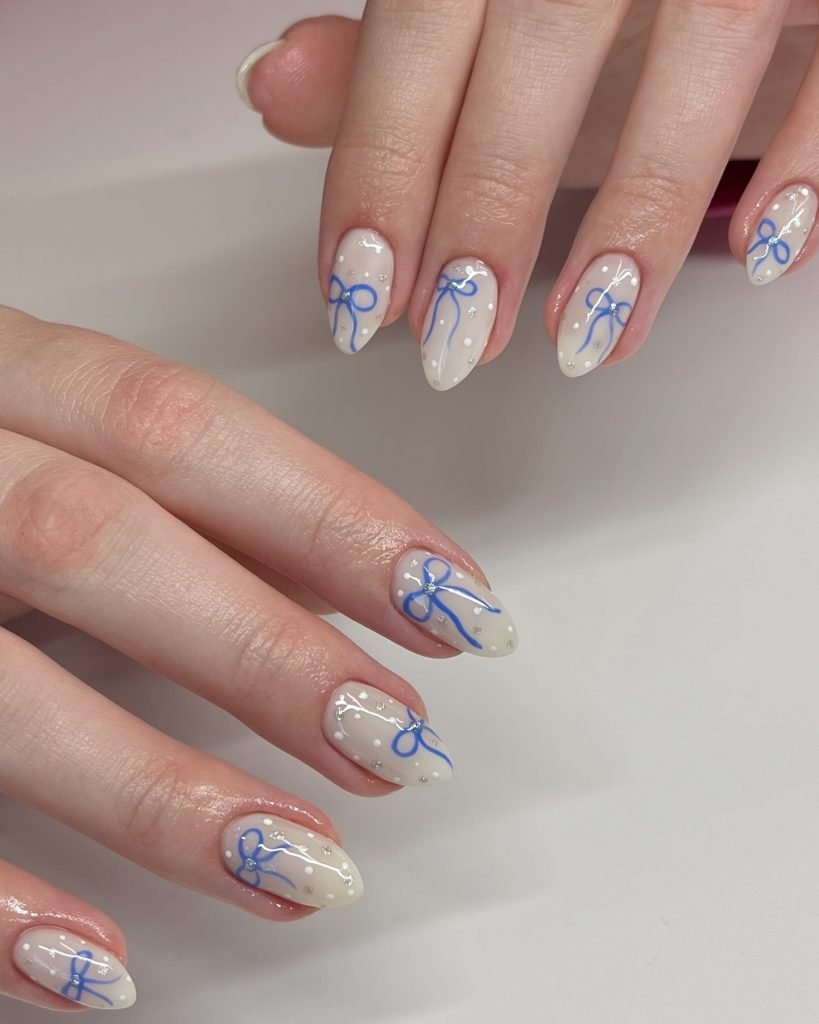 Elegant nail art with blue bows and white dots on almond-shaped nails.