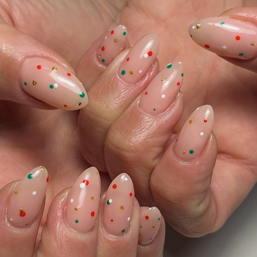 Festive polka dot nail art with pastel pink base featuring colorful dots including red, green, white, and gold accents.