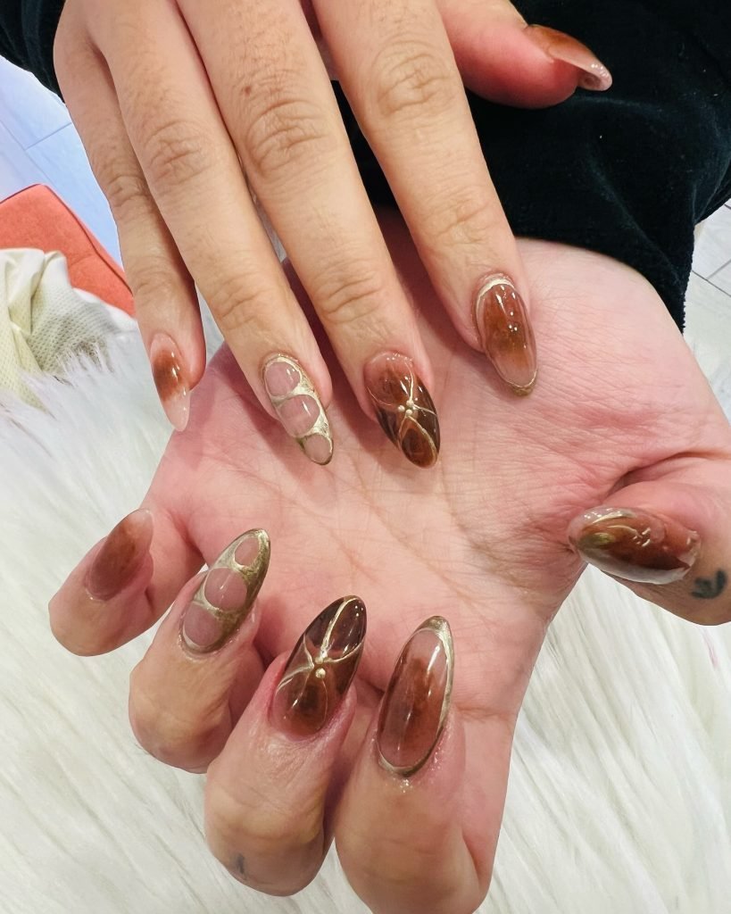 Almond-shaped nails with brown and gold abstract designs for a stylish, trendy manicure look.
