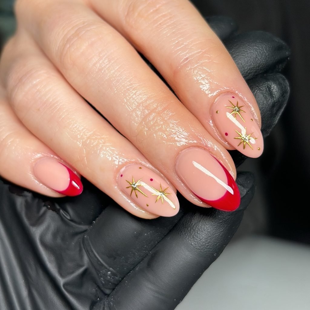 Elegant red and gold star nail art on a hand with black glove background, showcasing festive manicure style.