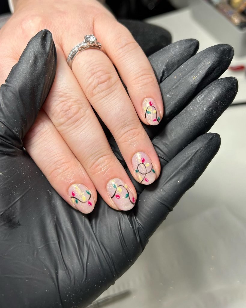 Festive nail art with colorful lights design on a hand wearing a ring, held by a gloved hand.