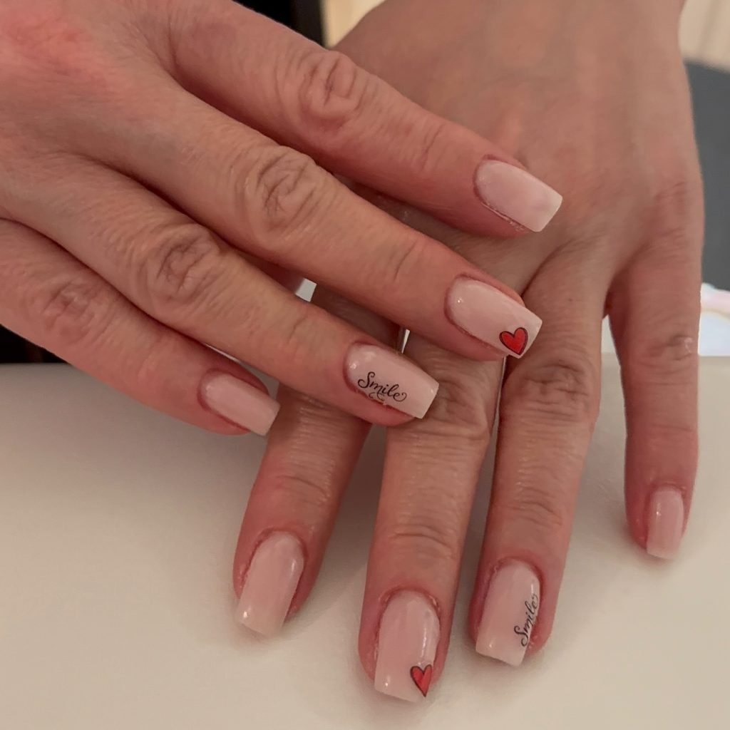 Neutral pink nails with heart and Smile designs, showcasing creative nail art.