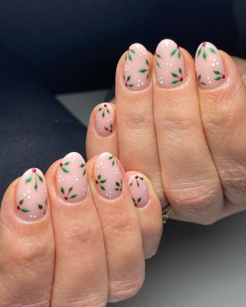 Festive nail art with tiny green leaves and red dots on pink polish, perfect for a holiday manicure.
