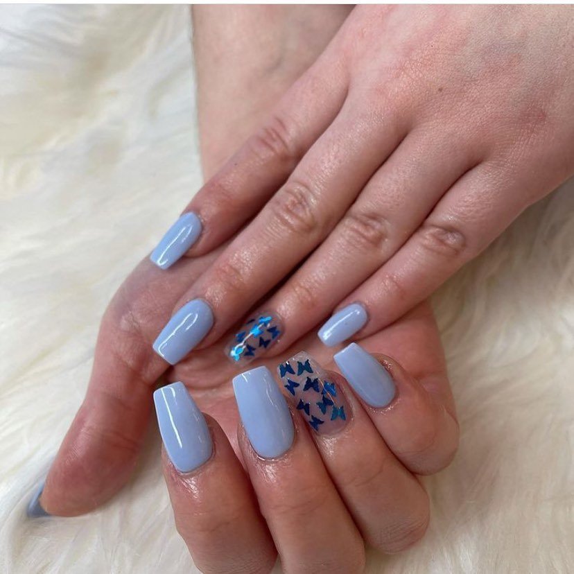 Close-up of hands with light blue nails and butterfly accents on a soft background. Stylish nail art design.