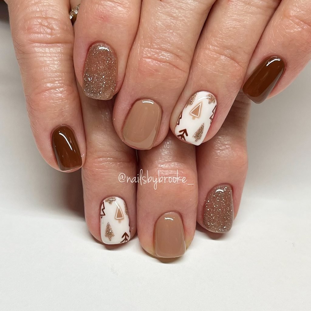 Close-up of autumn-themed manicure with brown, glitter, and white nails featuring geometric designs.