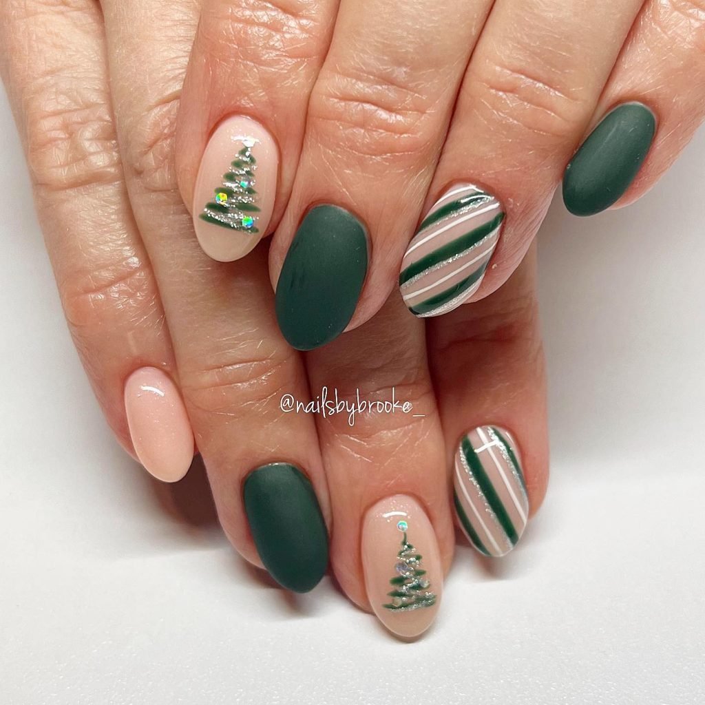 Festive green nail art with Christmas tree accents and striped designs on oval-shaped nails.