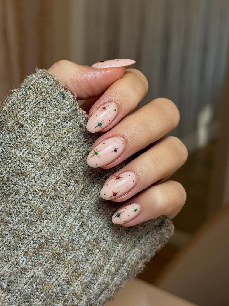 Stylish nude nails with colorful star nail art design held by a hand in a cozy gray sweater.