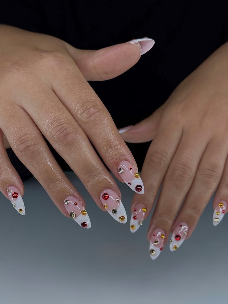 Stiletto nails with white nail art and colorful gem accents on both hands.