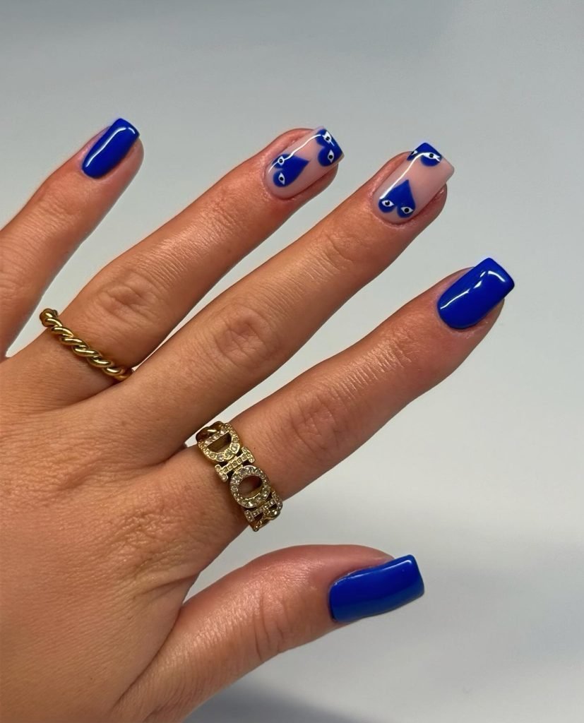 Blue nail art with geometric designs on manicured hand, featuring gold rings against a neutral background.