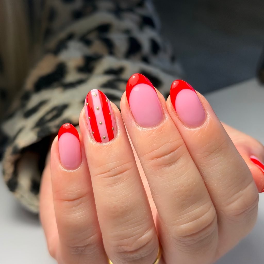 Stylish red and pink manicure with gold dotted accents on middle finger, featuring trendy French tips design.