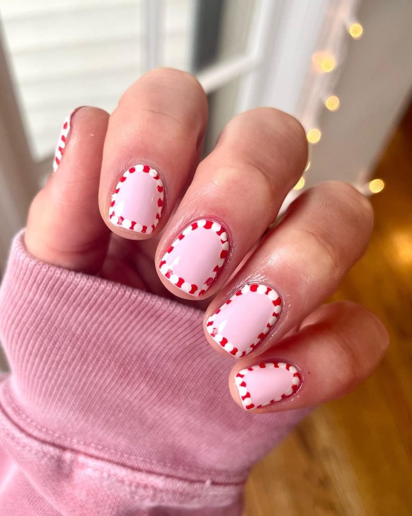 Close-up of a hand with pink nails featuring red dotted borders, wearing a pink sweater. Cozy, vibrant nail art.