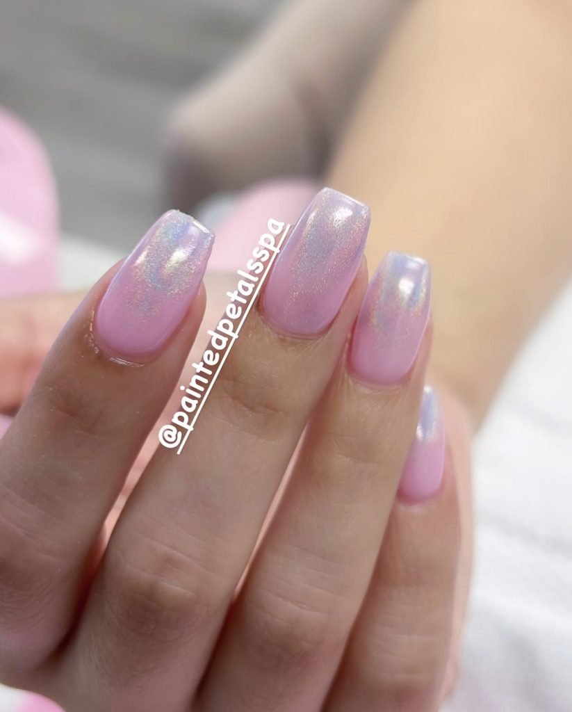 Close-up of a hand with pink chrome nails, showcasing a glossy and shimmering manicure.