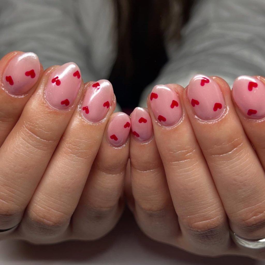 Pink nails with small red heart designs, perfect for Valentine's Day nail art inspiration.